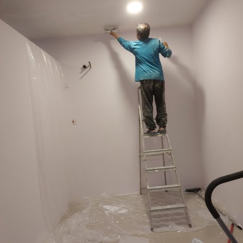 Person painting ceiling on ladder